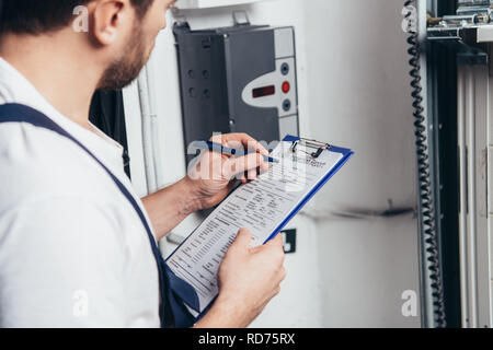 partial view of male electrician writing in clipboard and checking electrical box Stock Photo