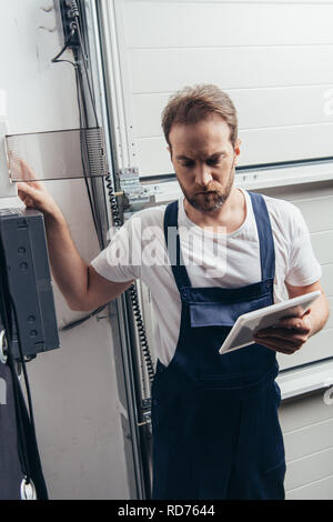 focused male bearded repairman with digital tablet checking electric box Stock Photo