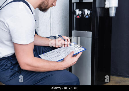 partial view of male repairman writing in clipboard during checking of broken water cooler Stock Photo