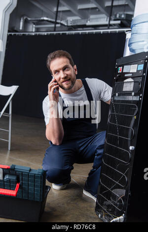 adult male craftsman talking on smartphone during repairing water cooler Stock Photo