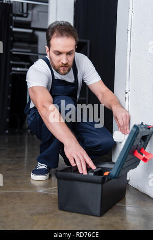 electrician in working overall taking tools from toolbox during repairing of plug socket Stock Photo