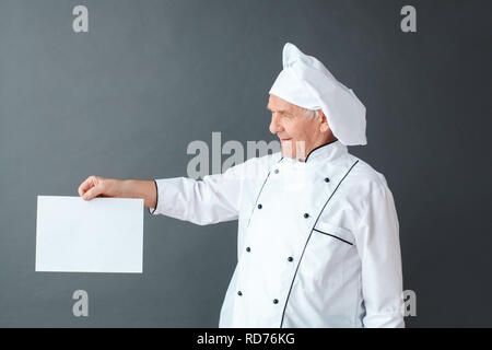 Senior chef studio standing isolated on gray looking at paper curious Stock Photo