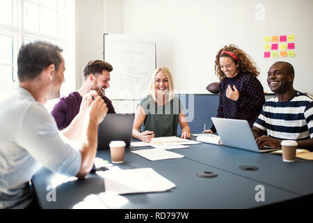 Smiling group of designers working on a project together while sitting around a boardroom table in an office Stock Photo