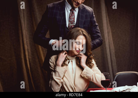 man putting pearl necklace on beautiful woman during romantic date in restaurant Stock Photo