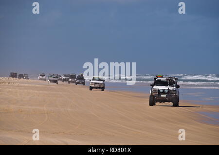 Line of four-wheel drives drive on beach next to choppy ocean