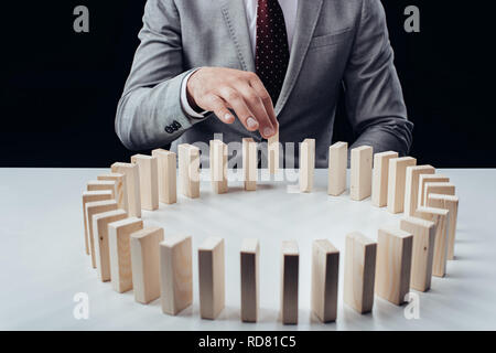 partial view of man picking wooden brick from row of blocks on desk isolated on black Stock Photo