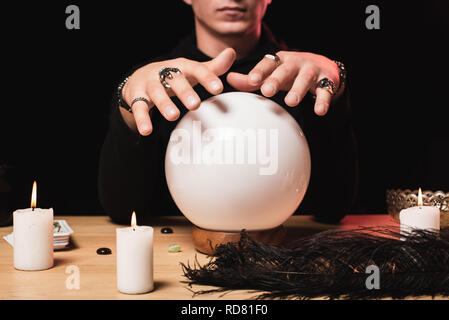 cropped view of man holding hands above crystal ball near candles isolated on black Stock Photo