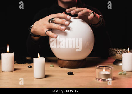 cropped view of esoteric holding hands above crystal ball near candles isolated on black Stock Photo