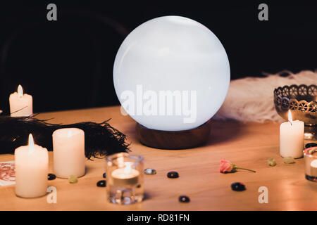 crystal ball near candles and feathers on wooden table isolated on black Stock Photo