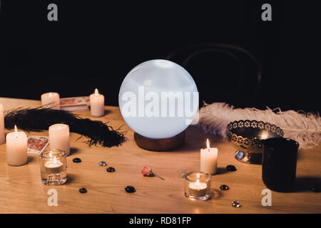 selective focus of crystal ball near candles and feathers on wooden table isolated on black Stock Photo
