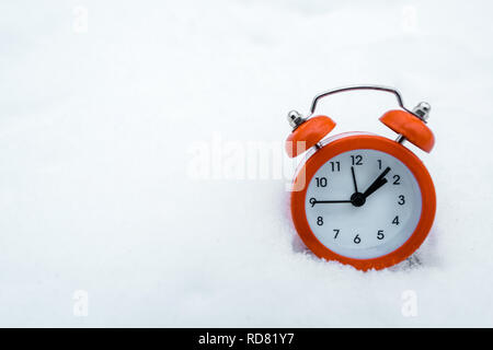 red retro alarm clock standing on white snow near trees in snowy forest Stock Photo