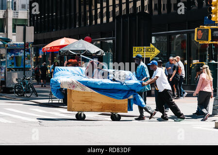 New York City, USA - June 26, 2018: Homeless pushing cart crossing street in Midtown of Manhattan. Stock Photo