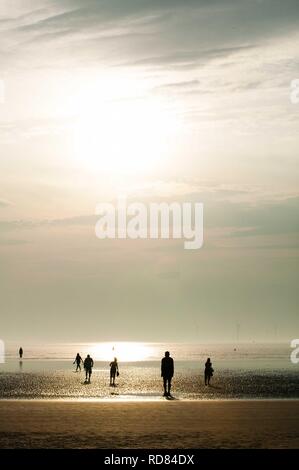 Sir Antony Gormley's sculpted figures , with tourists at sunset ,Another Place . Stock Photo