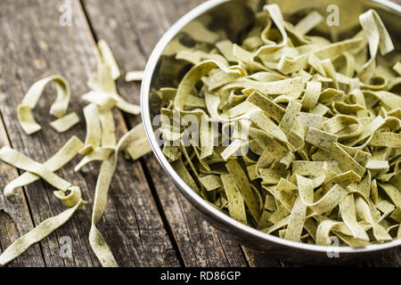 Raw italian pasta. Dry noodles with spinach in bowl. Stock Photo