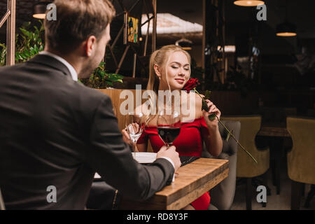 attractive woman smelling rose while sitting in restaurant with boyfriend Stock Photo