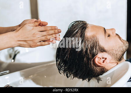 hands of young hairdresser washing hair to male client in beauty salon Stock Photo