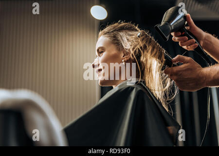 cropped shot of hairstylist drying hair to smiling girl in beauty salon Stock Photo