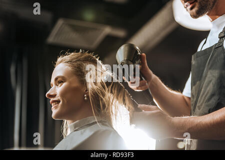 low angle view of hairstylist combing and drying hair to beautiful young woman in beauty salon Stock Photo
