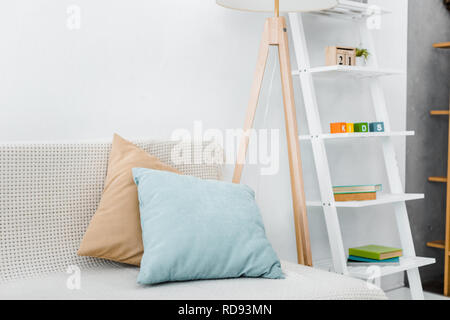 modern pillows on sofa near wooden lamp and toys on rack Stock Photo