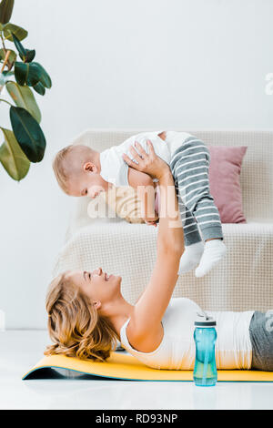 woman lying near plant and raising adorable child above head Stock Photo