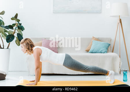 attractive woman doing push ups on yellow fitness mat near couch at home Stock Photo