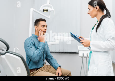 female dentist standing near  african american patient with toothache Stock Photo