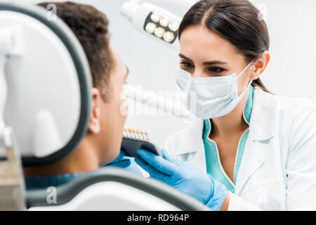 female dentist holding teeth color palette near african american patient Stock Photo