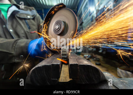 A close-up of a car mechanic using a metal grinder to cut   bearing in an auto repair shop, bright flashes flying in different directions. Work of aut Stock Photo
