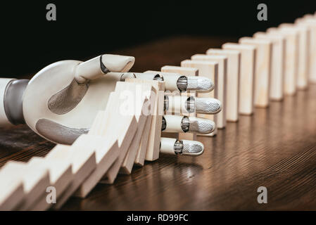 white robotic hand preventing wooden blocks from falling on desk Stock Photo