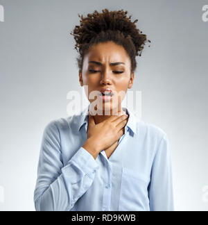 Throat pain. Woman holding her inflamed throat. Photo of african american woman in blue shirt on gray background. Medical concept Stock Photo