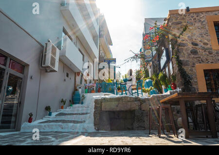 Kos, Greece - October 11, 2018: View of a side street in the city centre of the Greek city of Kos with bars and cafe tables and chairs. Stock Photo