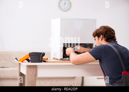 Young handsome contractor repairing fridge Stock Photo
