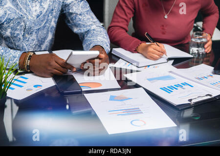 hands of dark-skinned people hold calculator against background of financial documents in business space closeup Stock Photo