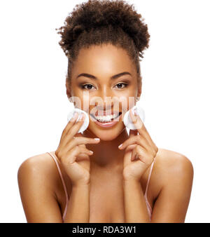 Charming young girl with flawless skin is holding cotton pads near face. Photo of smiling african american girl on white background. Skin care and bea Stock Photo