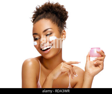Smiling woman with moisturizing cream on her face. Photo of african american woman with healthy skin isolated on white background. Beauty & Skin care  Stock Photo