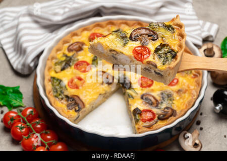 Baked homemade quiche pie in ceramic baking form and slice on wooden paddle Stock Photo