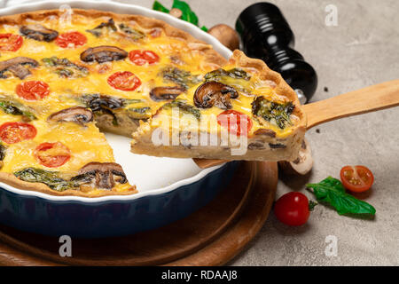 Baked homemade quiche pie in ceramic baking form and slice on wooden paddle Stock Photo