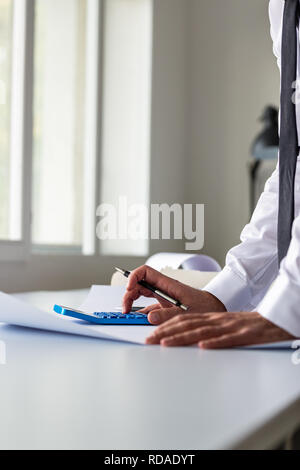 Businessman leaning on his office desk using calculator as he reviews paperwork and documentation. Stock Photo