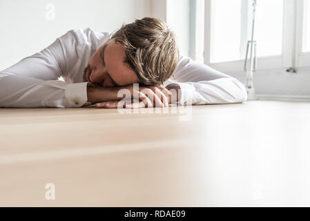 Tired businessman resting his head on his hands sitting at wooden office desk. With copy space on the lower part of the image. Stock Photo