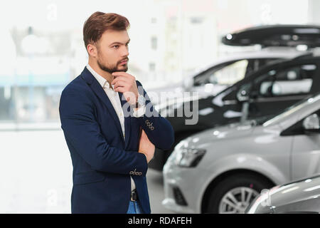 The buyer of the car thinks in the car dealership. A man looks at the car. Stock Photo