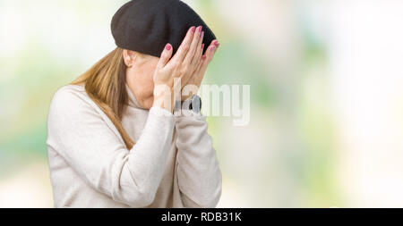 Middle age mature woman wearing winter sweater and beret over isolated background with sad expression covering face with hands while crying. Depressio Stock Photo