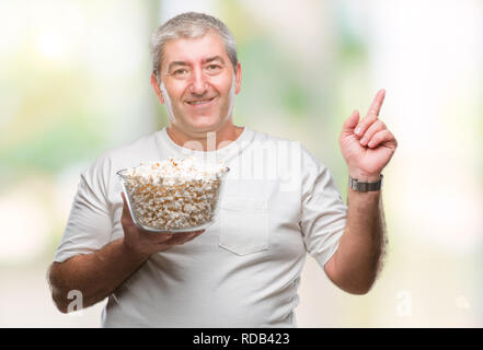 Handsome senior man eating popcorn over isolated background very happy pointing with hand and finger to the side Stock Photo