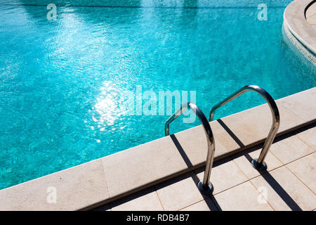 Metal handrail of swimming pool with stairs with fresh water in sunlight Stock Photo