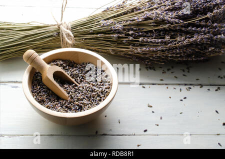 Bowl of dried herbal lavender flower buds with wooden scoop on white painted wood plank table. String tied bunch of stems behind. Stock Photo