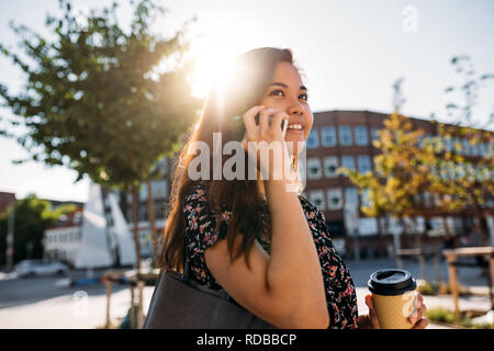 Smiling Asian university student walking and talking on her cellphone Stock Photo