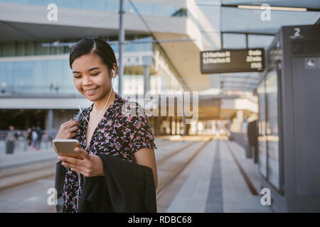 Smiling Asian student standing at a tram stop reading texts Stock Photo