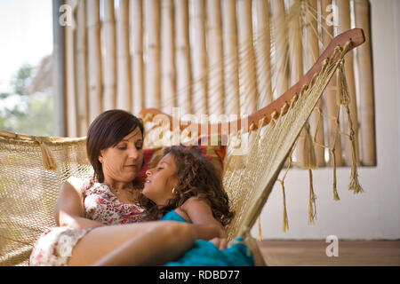 Mid-adult woman and her daughter lying in a hammock. Stock Photo