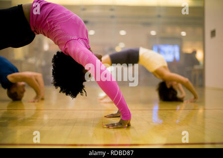 Young woman arching her back while on all fours in a yoga studio with two others. Stock Photo