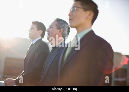 Three focused businessmen standing side by side outside in the sun. Stock Photo