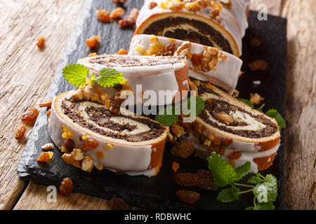 Poppy seed glazed roll, traditional Chistmas beigli cake on wooden table on black cutting board. Polish makowiec with candied fruits and nut. horizont Stock Photo